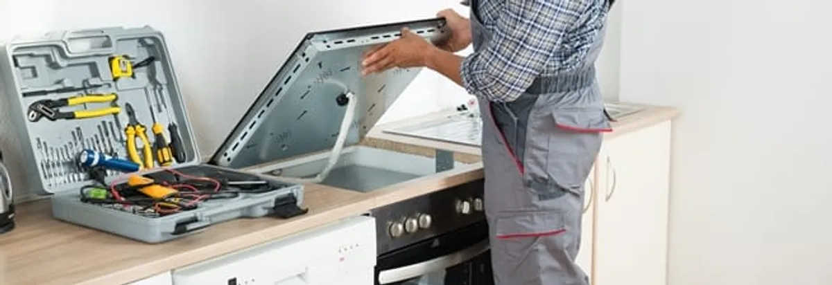 Cooktop repair technician lifting a built-in stovetop for service in Cincinnati, OH