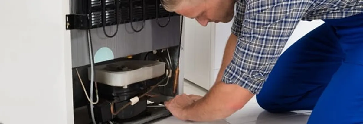 Refrigerator repair technician servicing the compressor and condenser area in Cincinnati, OH